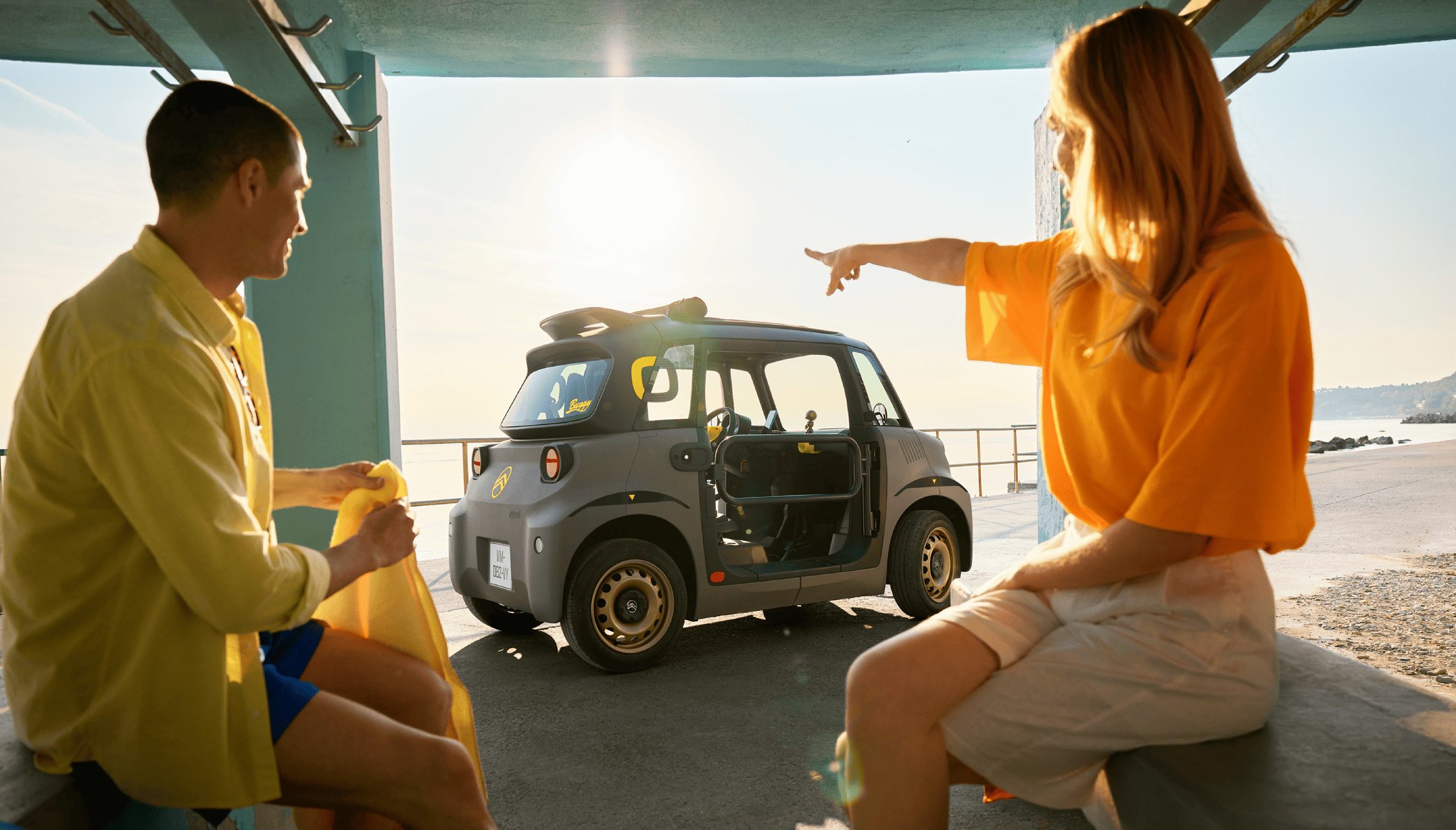 Vista laterale in spiaggia di Citroën Ami che mette in evidenza un design elettrico compatto e sicuro che interpreta la libertà estiva con semplicità e stile.